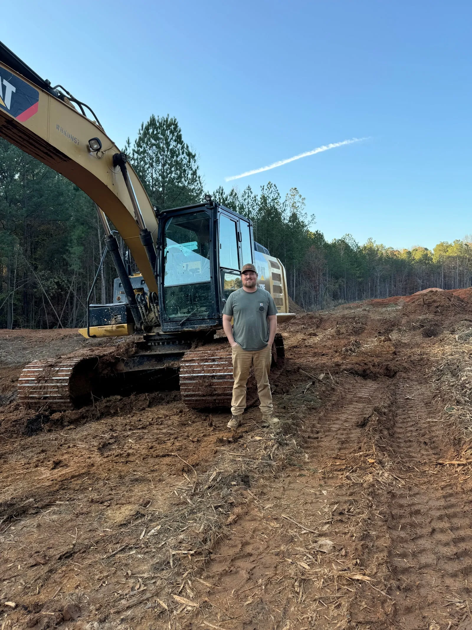 Ballard team member standing in front of a CAT excavator on a freshly cleared site